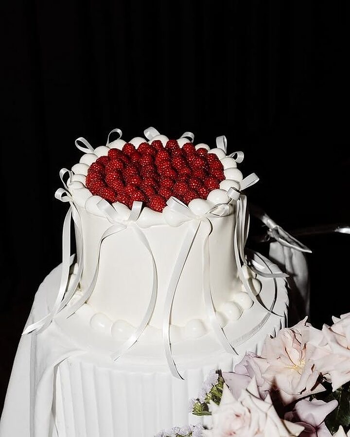 White wedding cake with sugar bows and raspberries at an evening reception