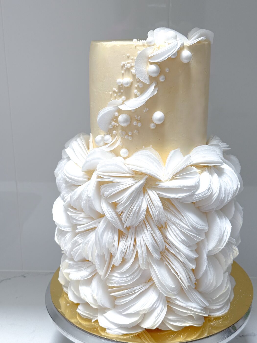Two-tier ivory wedding cake with wafer-petal ruffles and sugar pearls