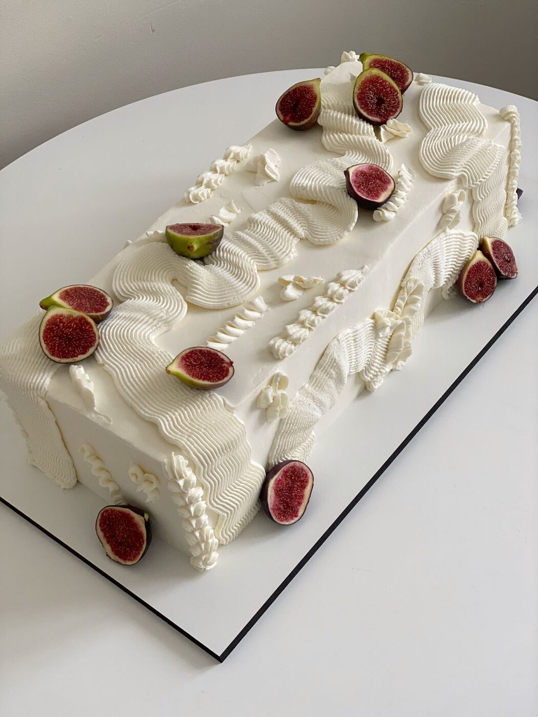 Long celebration cake piped with cream and topped with fresh figs