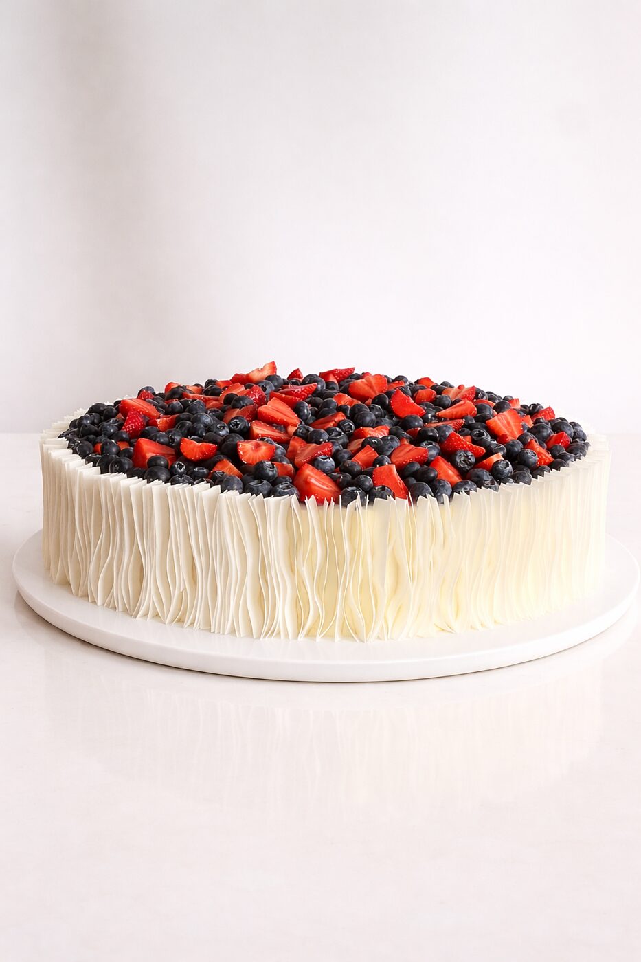 Round cake topped with strawberries and blueberries with ruffled sides