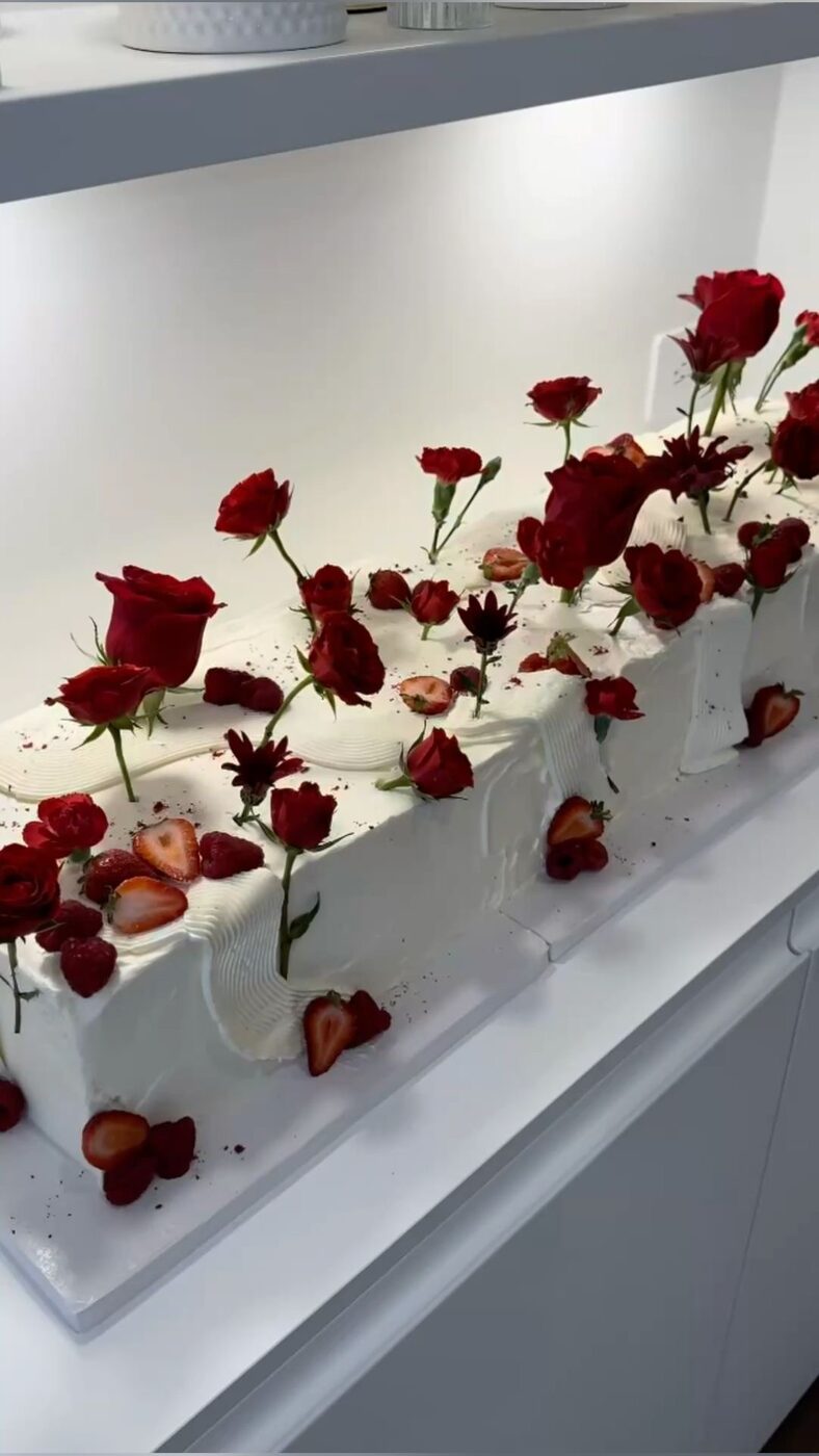 Long wedding cake dressed with red roses at the reception table
