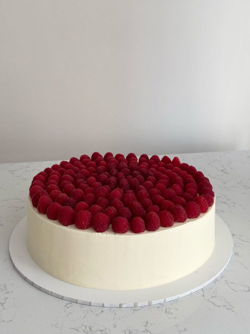 Round wedding cake covered with fresh raspberries
